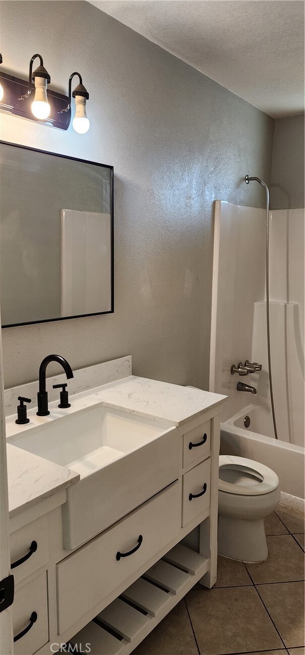 full bathroom featuring tile patterned floors, toilet, shower / bathing tub combination, vanity, and a textured ceiling