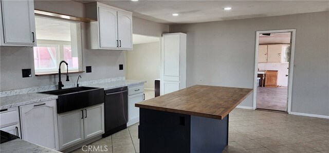 kitchen with light stone counters, a kitchen island, white cabinetry, dishwasher, and sink