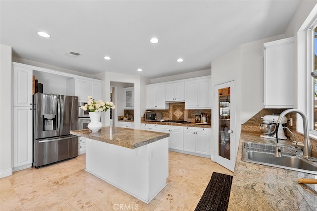 kitchen featuring light stone counters, a kitchen island, sink, stainless steel fridge with ice dispenser, and white cabinetry