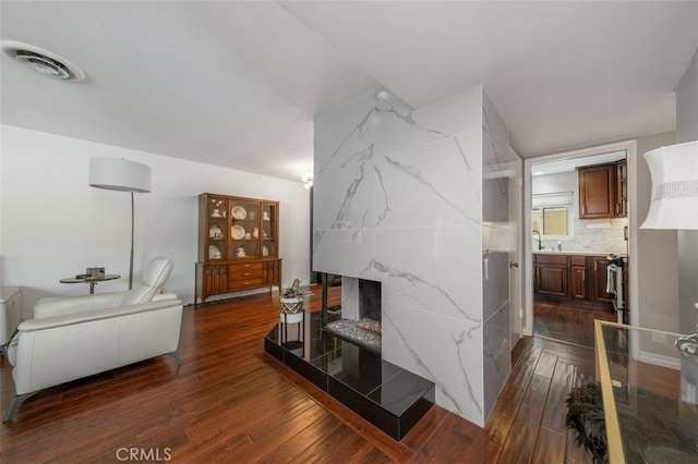 living room with dark wood-type flooring, a tiled fireplace, and sink