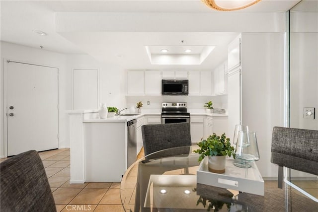 kitchen with sink, appliances with stainless steel finishes, a tray ceiling, light tile patterned flooring, and white cabinetry