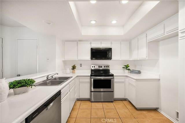 kitchen with appliances with stainless steel finishes, a tray ceiling, sink, light tile patterned floors, and white cabinets