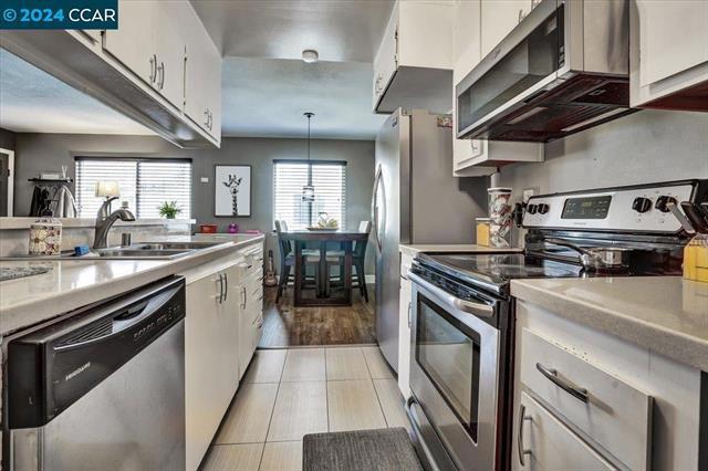 kitchen featuring stainless steel appliances, white cabinets, hanging light fixtures, and sink