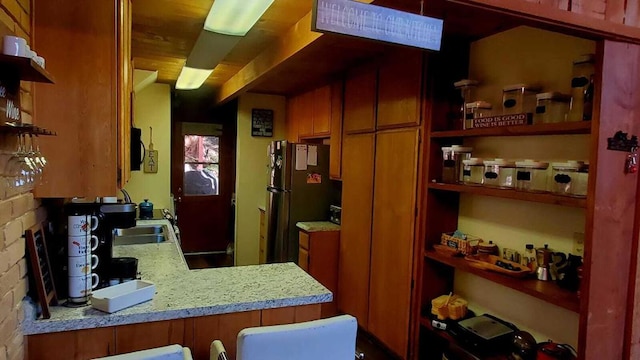 kitchen with stainless steel refrigerator, kitchen peninsula, sink, and light stone counters