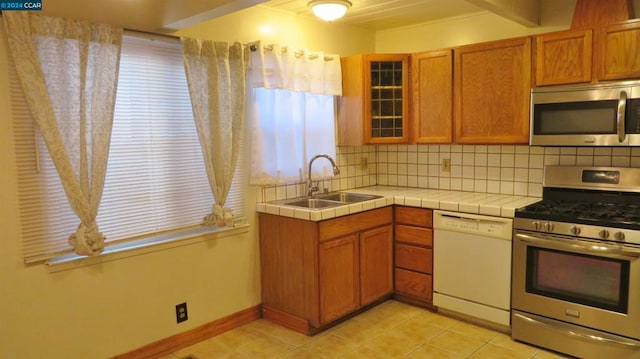 kitchen featuring decorative backsplash, stainless steel appliances, sink, light tile patterned floors, and tile countertops