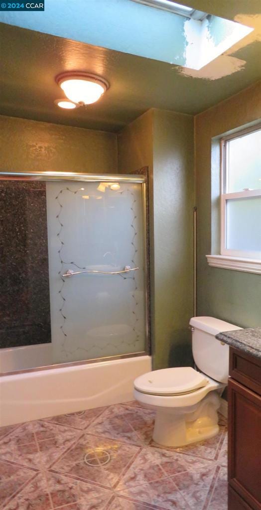 full bathroom with vanity, toilet, combined bath / shower with glass door, and a skylight