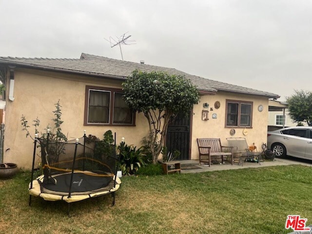 back of property featuring a patio, a yard, and a trampoline