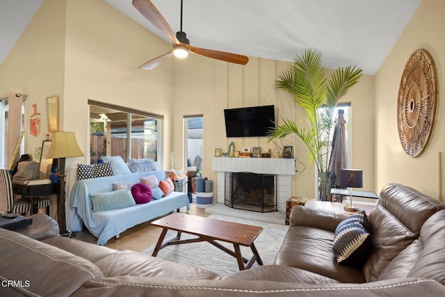 living room featuring ceiling fan, a fireplace, high vaulted ceiling, and light wood-type flooring