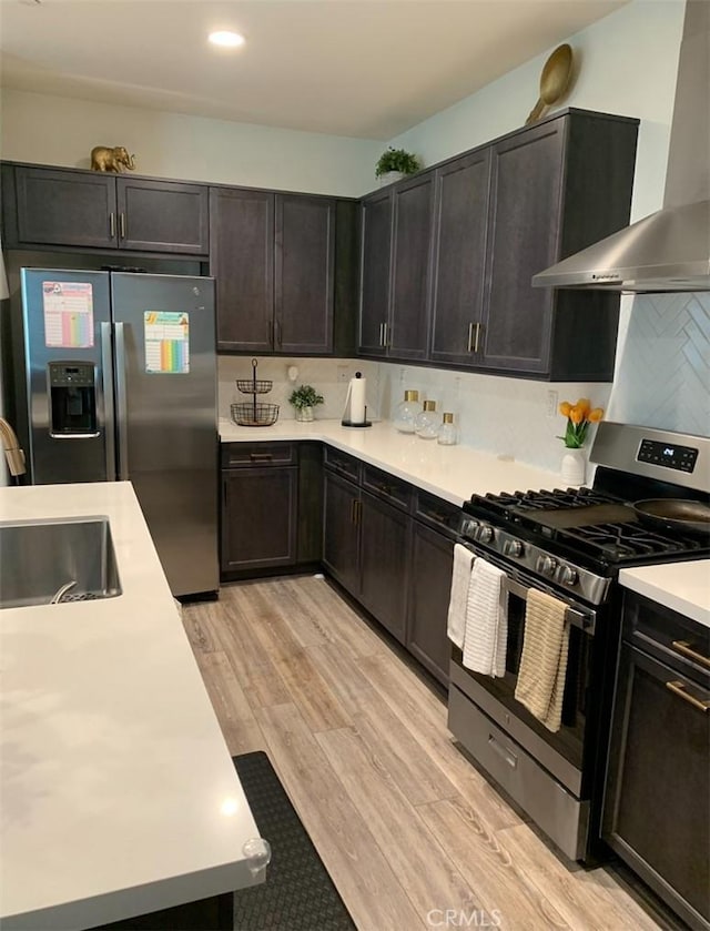 kitchen featuring sink, light hardwood / wood-style flooring, wall chimney exhaust hood, decorative backsplash, and stainless steel appliances