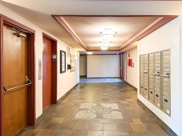 hallway with a raised ceiling, elevator, mail boxes, and a textured ceiling