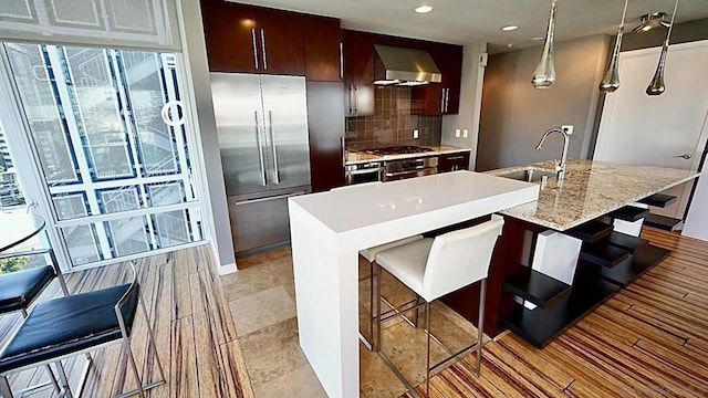 kitchen featuring a center island with sink, wall chimney range hood, sink, and stainless steel appliances