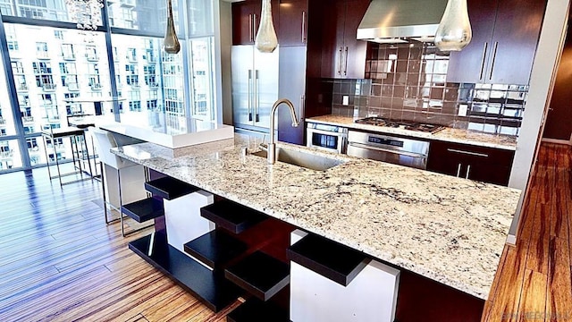 kitchen with sink, stainless steel appliances, backsplash, decorative light fixtures, and light wood-type flooring