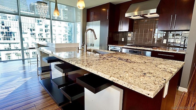 kitchen featuring pendant lighting, dark wood-type flooring, wall chimney exhaust hood, decorative backsplash, and stainless steel gas cooktop