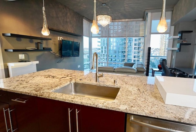 kitchen featuring stainless steel dishwasher, decorative light fixtures, light stone counters, and sink