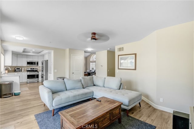 living room with ceiling fan, sink, and light wood-type flooring