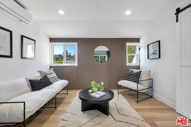 living room with a wall mounted air conditioner, a barn door, light hardwood / wood-style floors, and a wealth of natural light