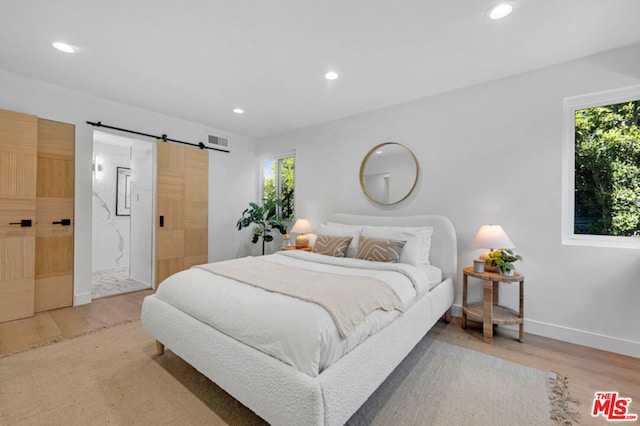 bedroom featuring hardwood / wood-style floors, a barn door, multiple windows, and ensuite bath