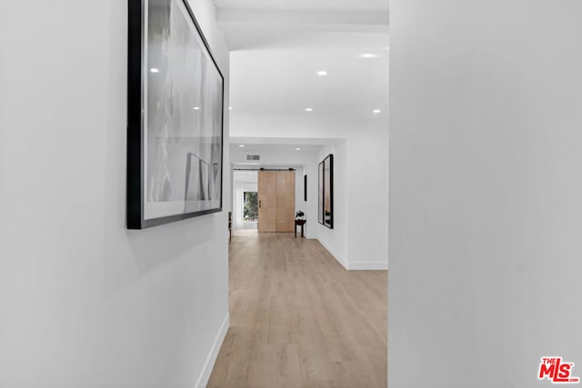 hallway with a barn door and light hardwood / wood-style flooring