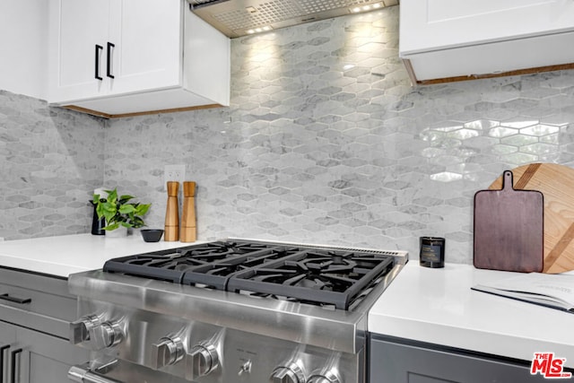 kitchen with tasteful backsplash, white cabinetry, exhaust hood, and stainless steel range oven