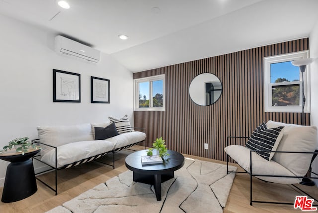 sitting room with light hardwood / wood-style floors, an AC wall unit, and vaulted ceiling