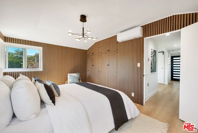 bedroom with a notable chandelier, light hardwood / wood-style floors, an AC wall unit, and vaulted ceiling