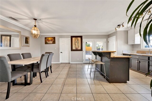 tiled dining space featuring a notable chandelier, ornamental molding, sink, and french doors