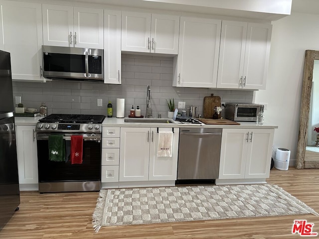 kitchen featuring backsplash, white cabinets, light wood-type flooring, and appliances with stainless steel finishes