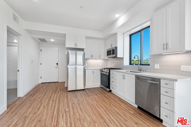 kitchen with sink, decorative backsplash, light hardwood / wood-style floors, white cabinetry, and stainless steel appliances