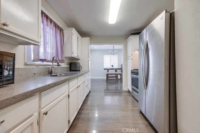 kitchen featuring stainless steel appliances, sink, light hardwood / wood-style flooring, an inviting chandelier, and white cabinetry