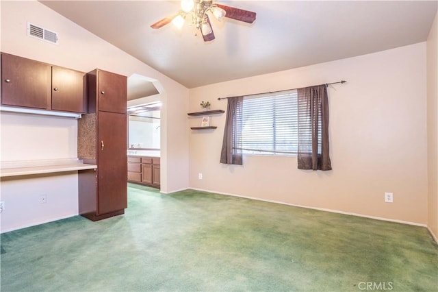 unfurnished living room featuring dark colored carpet, built in desk, ceiling fan, and lofted ceiling