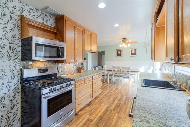 kitchen with light wood-type flooring, backsplash, stainless steel appliances, ceiling fan, and sink