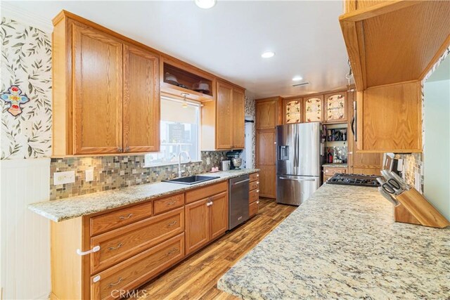 kitchen featuring backsplash, sink, light stone countertops, light wood-type flooring, and stainless steel appliances