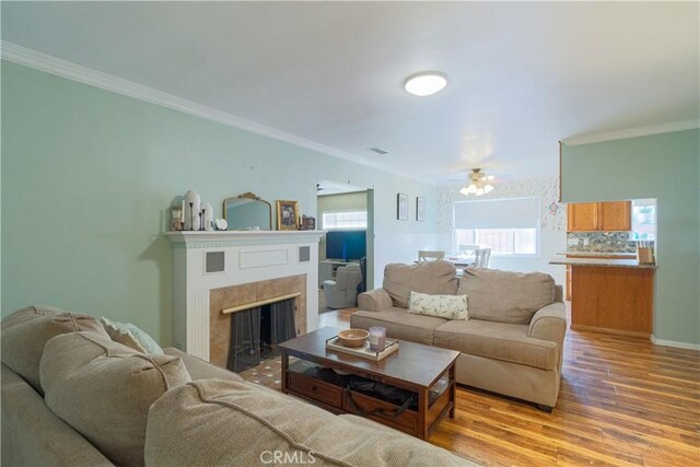 living room featuring a tiled fireplace, ceiling fan, hardwood / wood-style floors, and crown molding