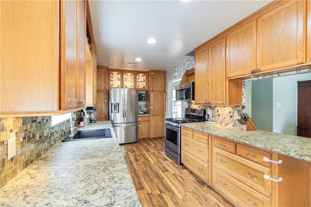 kitchen with light stone countertops, sink, stainless steel appliances, light hardwood / wood-style floors, and decorative backsplash