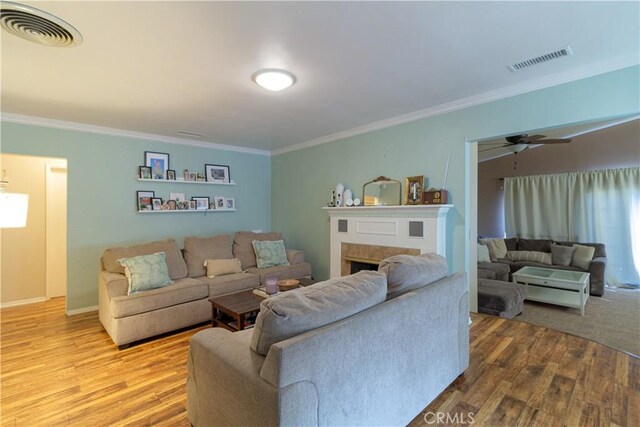 living room featuring wood-type flooring, ceiling fan, and crown molding