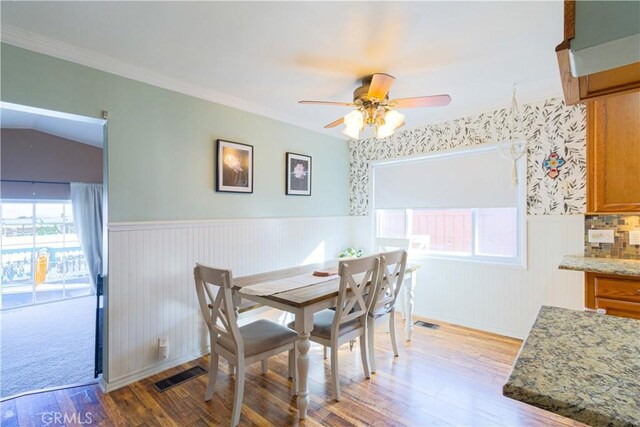 dining room with ceiling fan, light wood-type flooring, ornamental molding, and vaulted ceiling