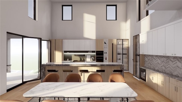 kitchen with light hardwood / wood-style floors, a healthy amount of sunlight, a high ceiling, and a kitchen breakfast bar