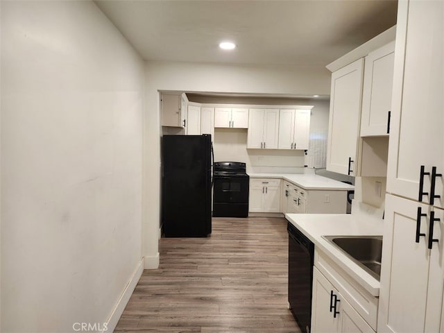 kitchen with sink, black appliances, wood-type flooring, and white cabinets