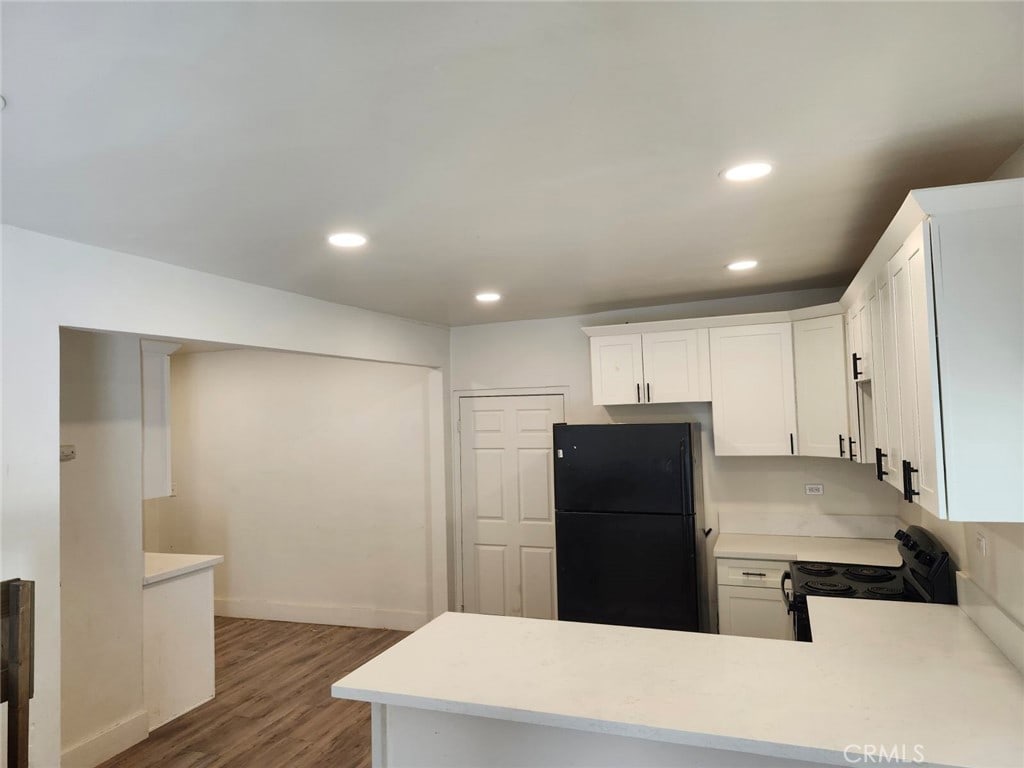 kitchen with black appliances, white cabinets, kitchen peninsula, and dark hardwood / wood-style floors