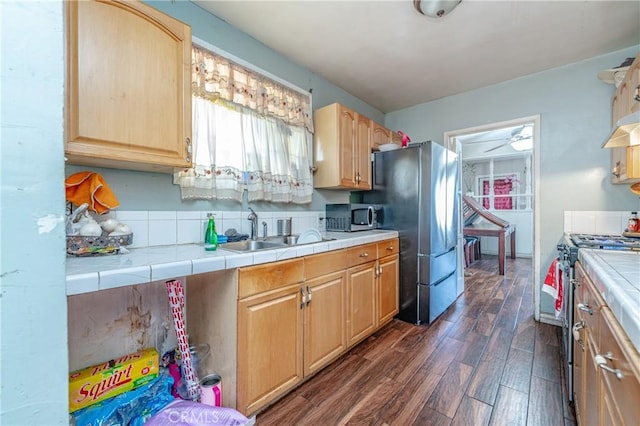 kitchen with appliances with stainless steel finishes, tile counters, dark wood-type flooring, light brown cabinets, and sink