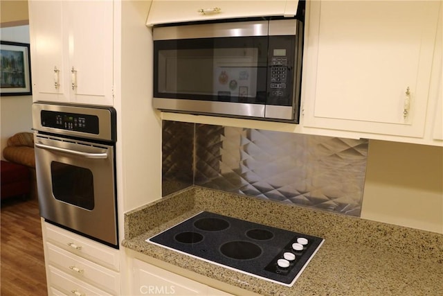 kitchen with backsplash, white cabinets, appliances with stainless steel finishes, light stone counters, and wood-type flooring