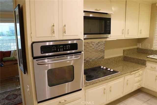 kitchen featuring light stone countertops, ornamental molding, appliances with stainless steel finishes, light tile patterned flooring, and white cabinetry