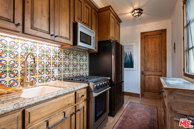 kitchen featuring stainless steel appliances, backsplash, sink, light stone countertops, and light tile patterned flooring