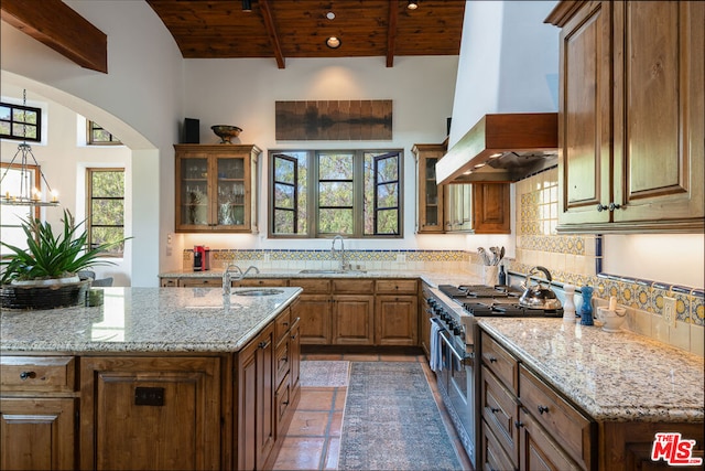 kitchen featuring beam ceiling, wooden ceiling, custom range hood, range with two ovens, and sink