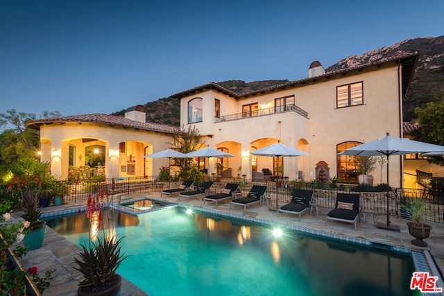 back house at dusk with a patio area, a balcony, and a swimming pool with hot tub