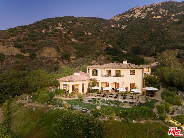 back of house with a balcony, a swimming pool, a mountain view, and a patio