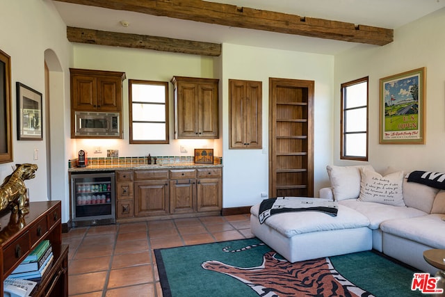 living room with dark tile patterned flooring, wet bar, beamed ceiling, and beverage cooler