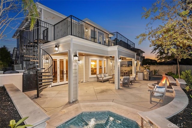 back house at dusk with french doors, a balcony, an outdoor living space with a fire pit, and a patio area