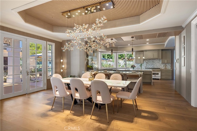 dining space featuring a tray ceiling, ornamental molding, and light wood-type flooring