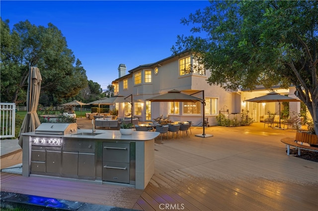 deck at dusk featuring an outdoor kitchen, area for grilling, and exterior bar